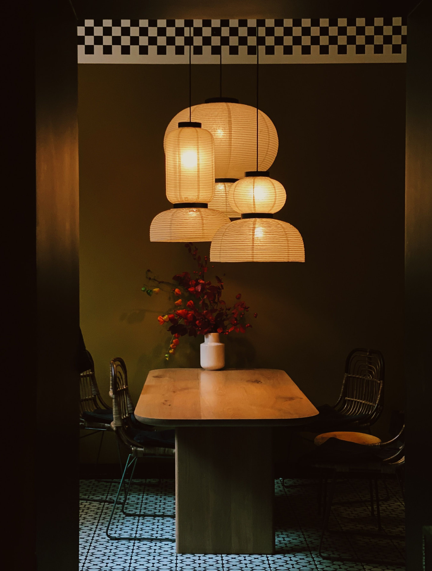 Intieme eetruimte met een houten tafel, rotan stoelen en hanglampen van rijstpapier die een warm licht werpen op een witte vaas met herfsttakken